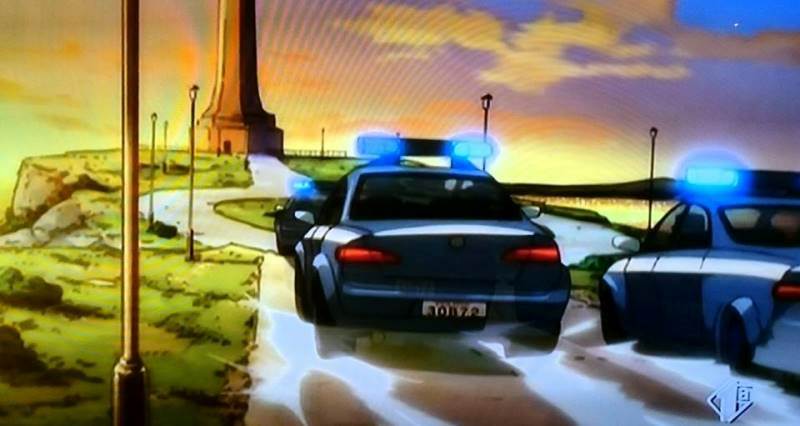 Le auto della Polizia inseguono Lupin; in lontananza si nota la torre campanara del porto