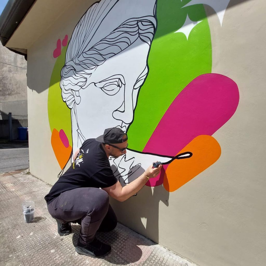 Artist painting a mural with colorful abstract shapes and a classical figure